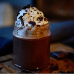 A glass filled with vegan hot chocolate topped with whipped cream and shaved chocolate