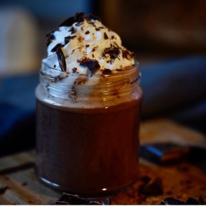 A glass filled with vegan hot chocolate topped with whipped cream and shaved chocolate