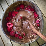 a bowl of vegan chocolate nice cream topped with raspberries and cacao nibs