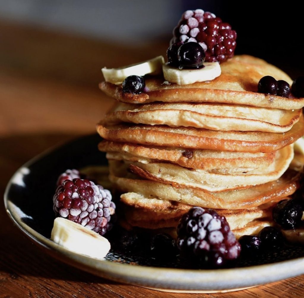A stack of vegan banana pancakes on a plate topped with berries and banana
