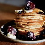 A stack of vegan banana pancakes on a plate topped with berries and banana