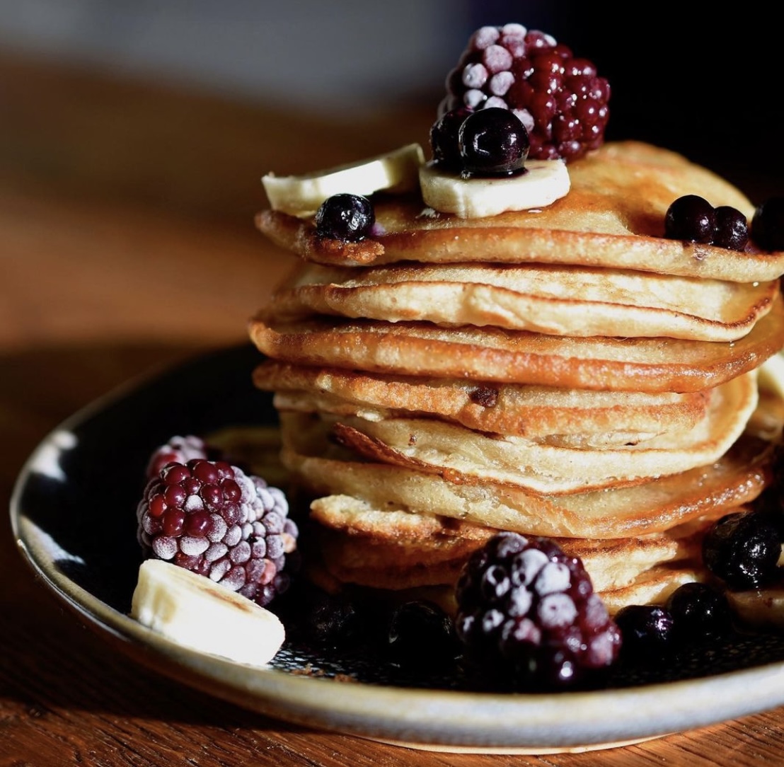 A stack of vegan banana pancakes on a plate topped with berries and banana
