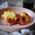 vegan shepherd's pie on a blush pink plate decorated with herbs