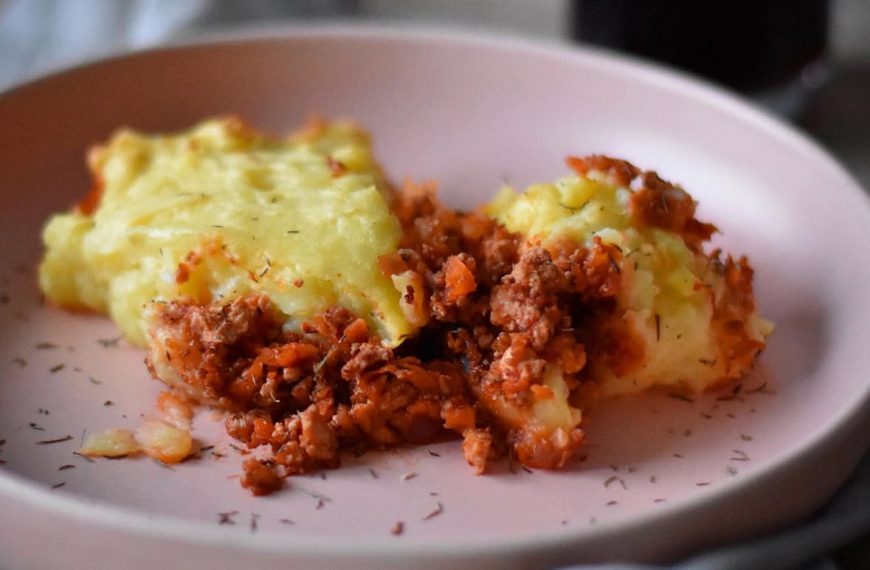 vegan shepherd's pie on a blush pink plate decorated with herbs