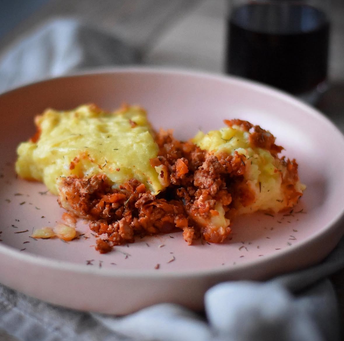 vegan shepherd's pie on a blush pink plate decorated with herbs