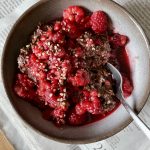 vegan chocolate oatmeal topped with lots of fresh raspberries in a small bowl on top of a newspaper