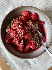 vegan chocolate oatmeal topped with lots of fresh raspberries in a small bowl on top of a newspaper