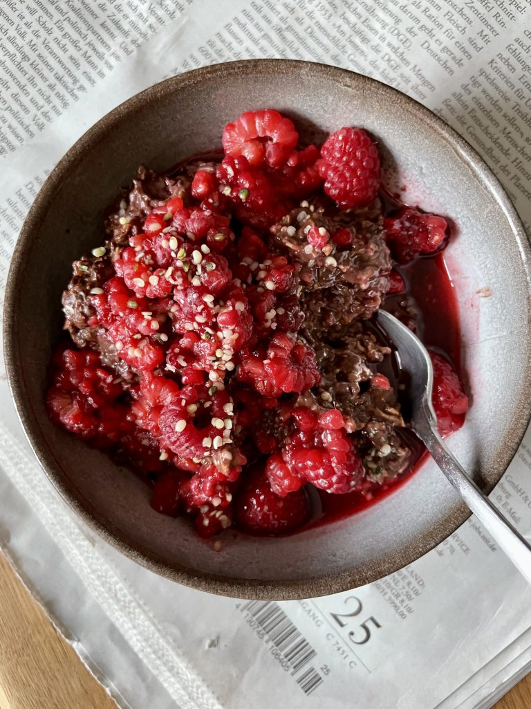 vegan chocolate oatmeal topped with lots of fresh raspberries in a small bowl on top of a newspaper