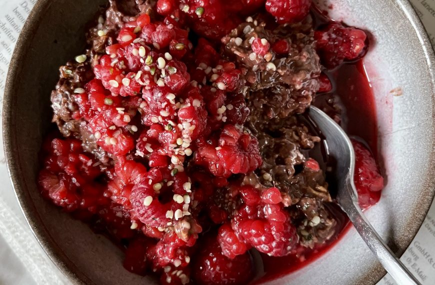 vegan chocolate oatmeal topped with lots of fresh raspberries in a small bowl on top of a newspaper