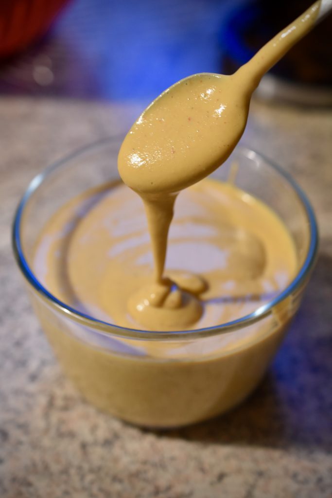 vegan cheesy sauce on a spoon over a glass bowl filled with vegan cheese sauce
