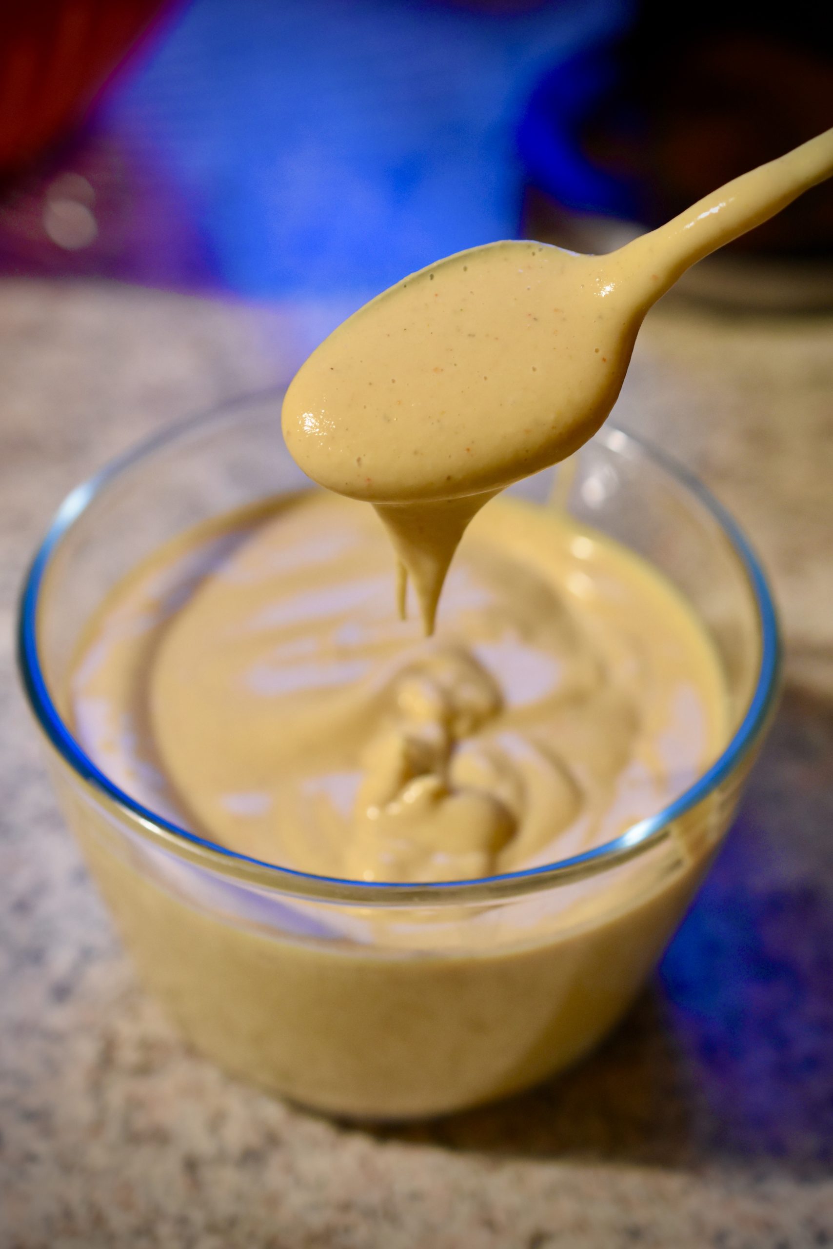 Vegan cheesy sauce on a spoon over a glass bowl on a counter