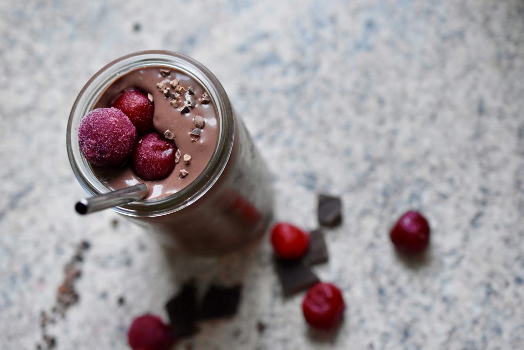 a thick, creamy vegan chocolate cherry smoothie decorated with frozen cherries and cacao nibs in a glass with a metal straw