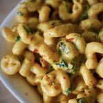 a close-up of curly pasta with vegan cheesy sauce, spinach, and chili flakes