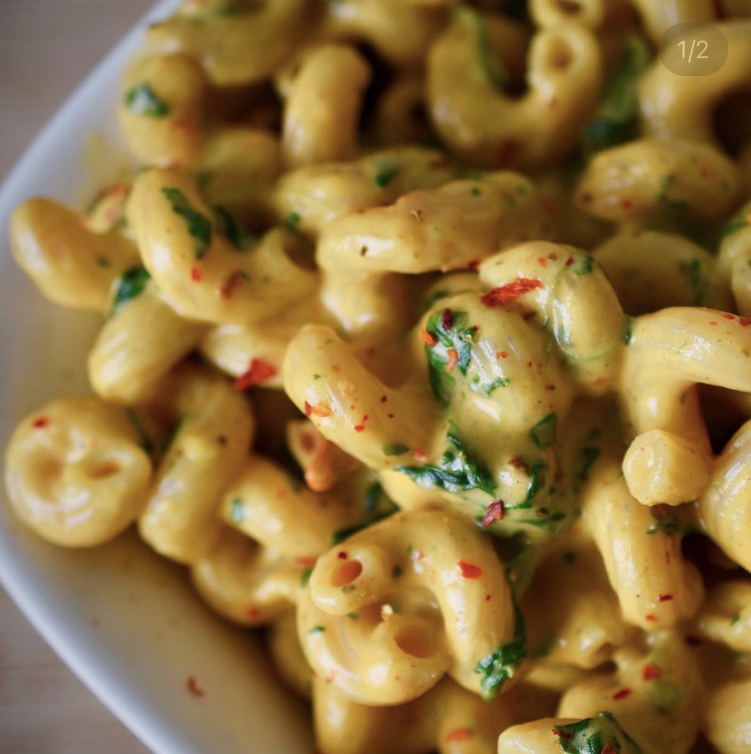 a close-up of curly pasta with vegan cheesy sauce, spinach, and chili flakes
