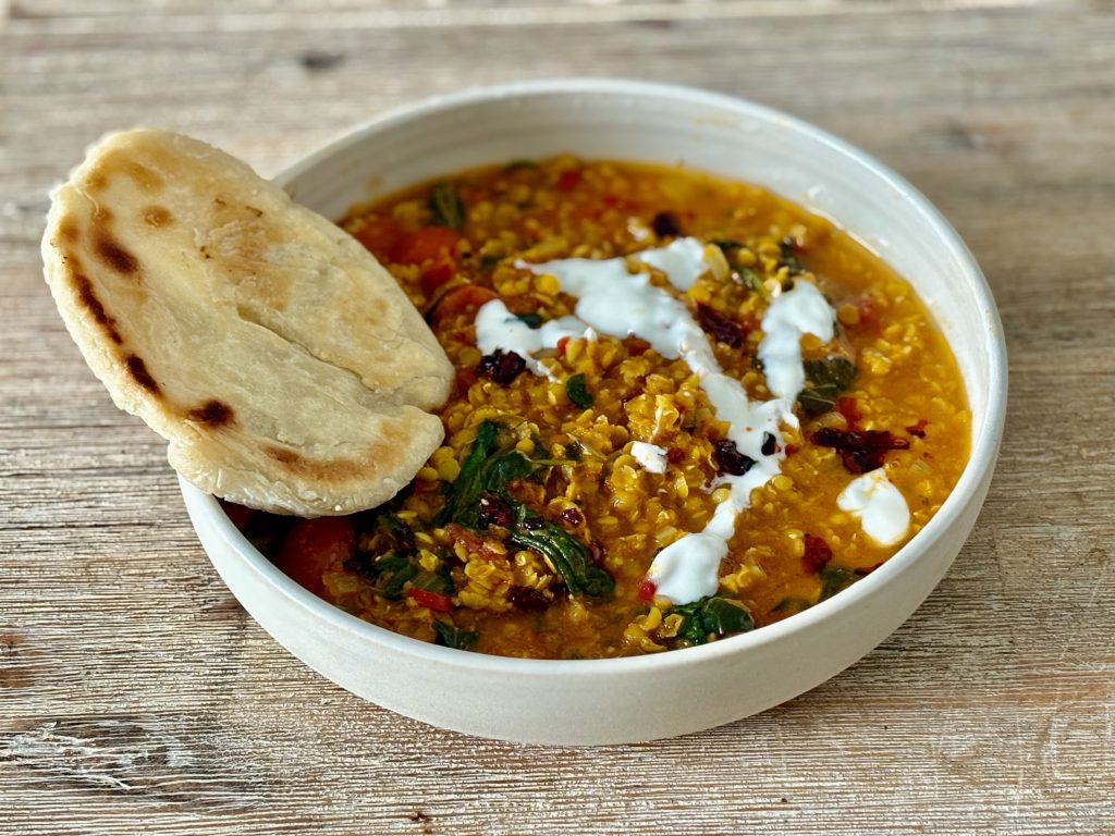 vegan red lentil dal on a plate with homemade naan bread and topped with vegan yogurt
