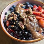 a bowl of vegan oatmeal with berries, almond butter, and pecans