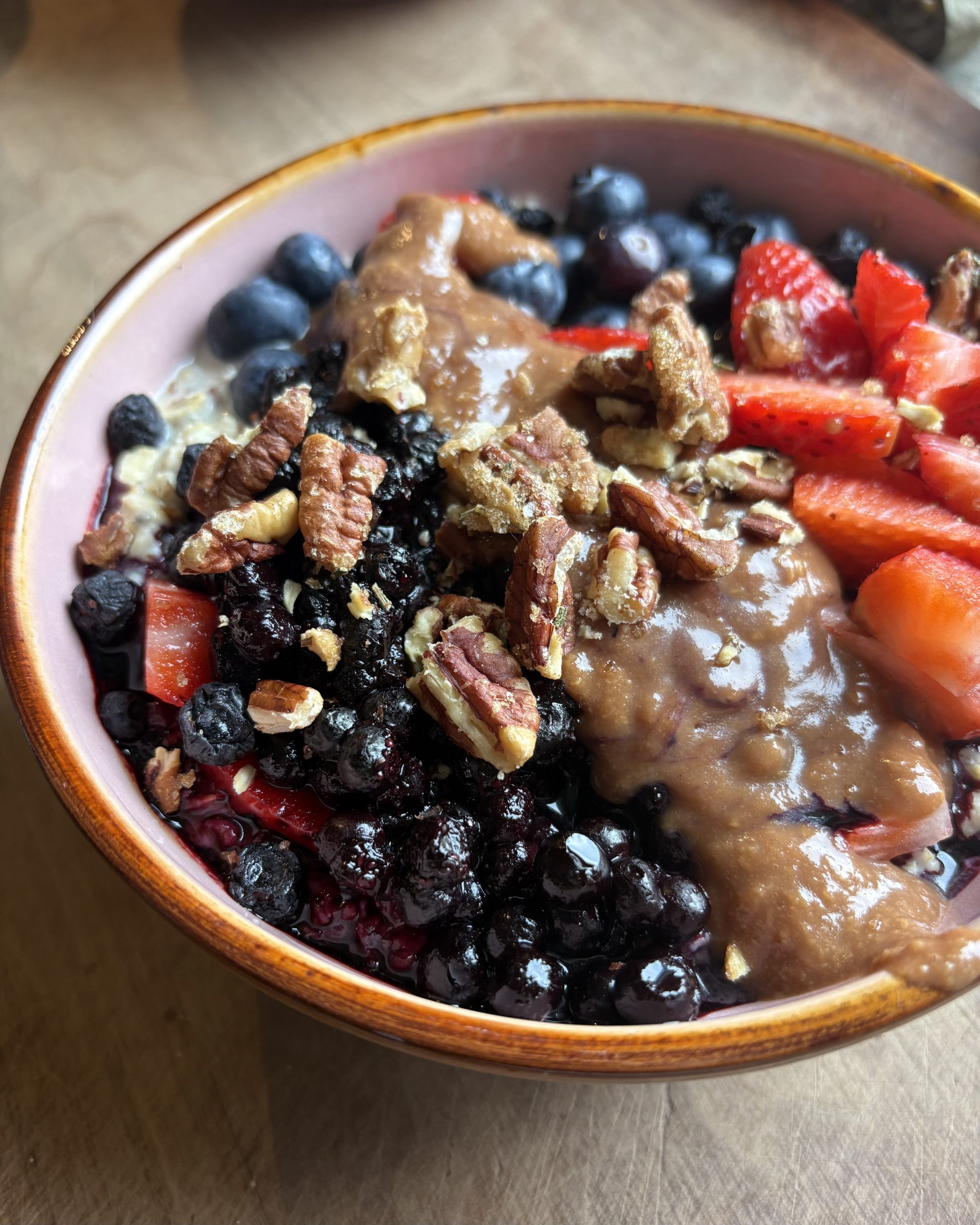 a bowl of vegan oatmeal with berries, almond butter, and pecans