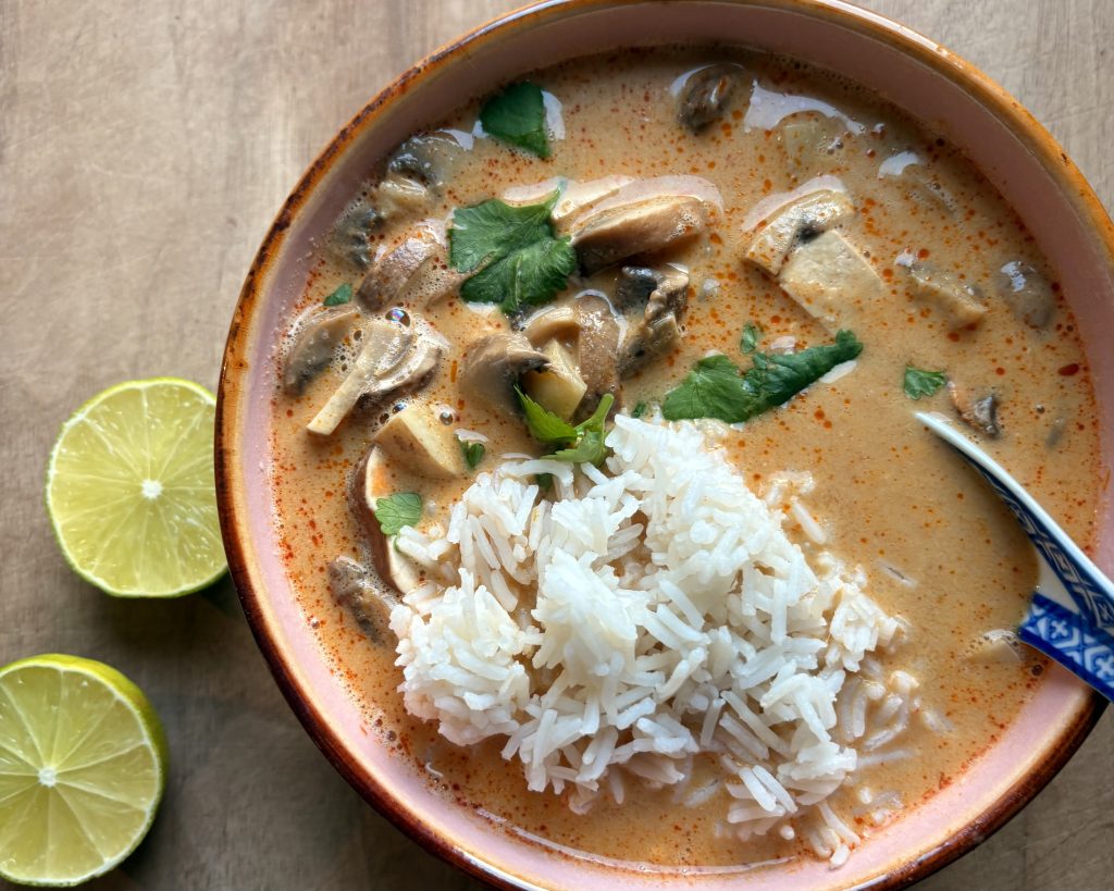 vegan tom yum soup with mushrooms and tofu in a bowl with limes